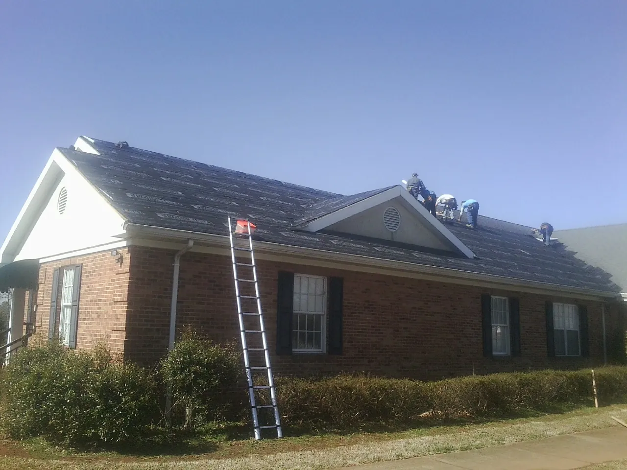Crew tearing shingles off a brick ranch roof with a ladder set — Metal Roof Repair work by our crew in Yoncalla