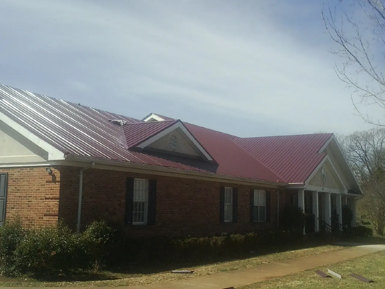 Red metal roof with gabled entries on a long brick building, from a Hail Damage Roof Repair job in Yoncalla