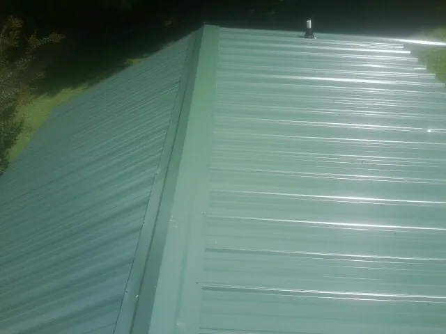 New green metal panels meeting at the ridge of a roof — Flat Roof Repair work by our crew in Yoncalla