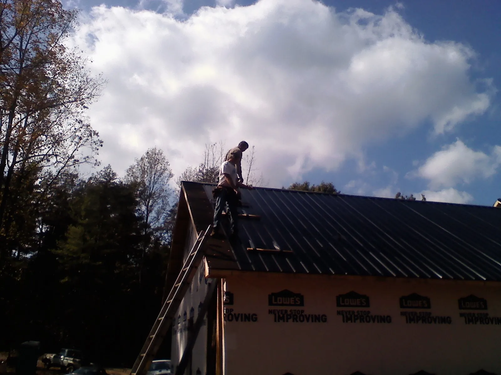 Roofer fastening dark metal panels high against a cloudy sky, from a Roof Inspection job in Yoncalla